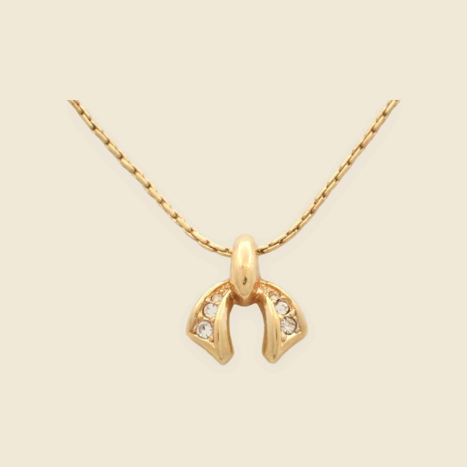 Collana Christian Dior in metallo dorato, con catena sottile e pendente arcuato ornato da pietre chiare su fondo neutro