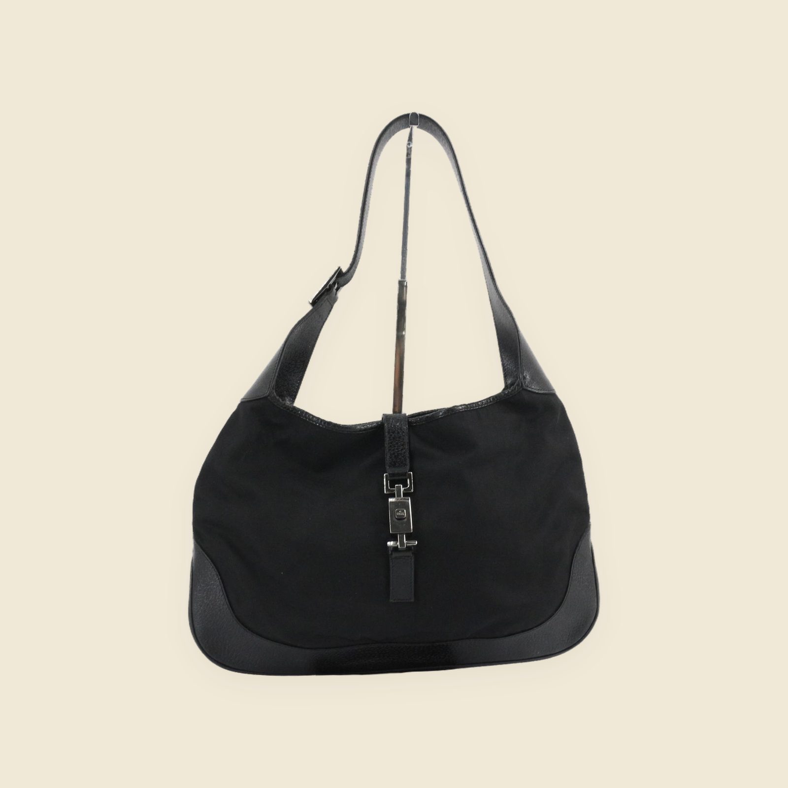 Borsa a spalla Gucci in tela e pelle nera, a mezzaluna, con chiusura a pistone, vista frontale su fondo bianco