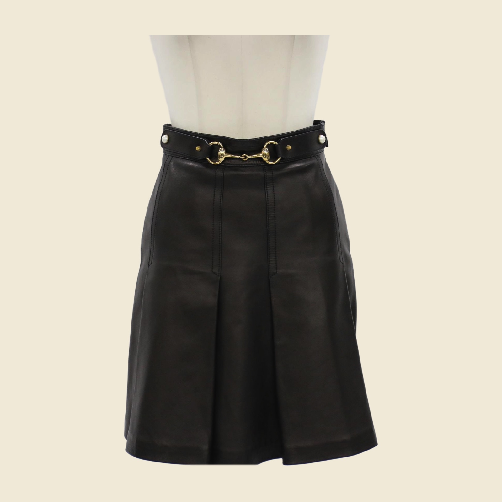 Gonna Gucci in pelle nera a pieghe con morsetto dorato e cintura con borchie e perle, vista frontale su manichino