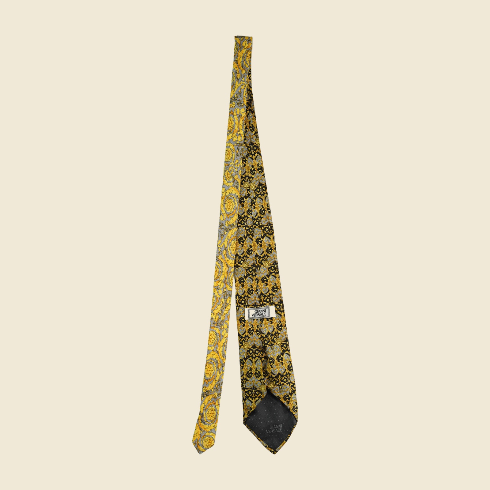 Cravatta Gianni Versace barocca a pannello, volute d'acanto e mascheroni in oro su fondo nero e grigio argento, vista frontale su fondo neutro