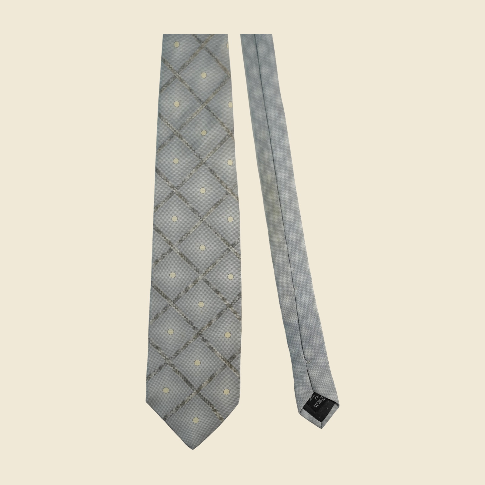 Cravatta Gianni Versace in seta grigio argento, reticolo diagonale di greca a rombi con pois avorio, su fondo neutro — vista 2