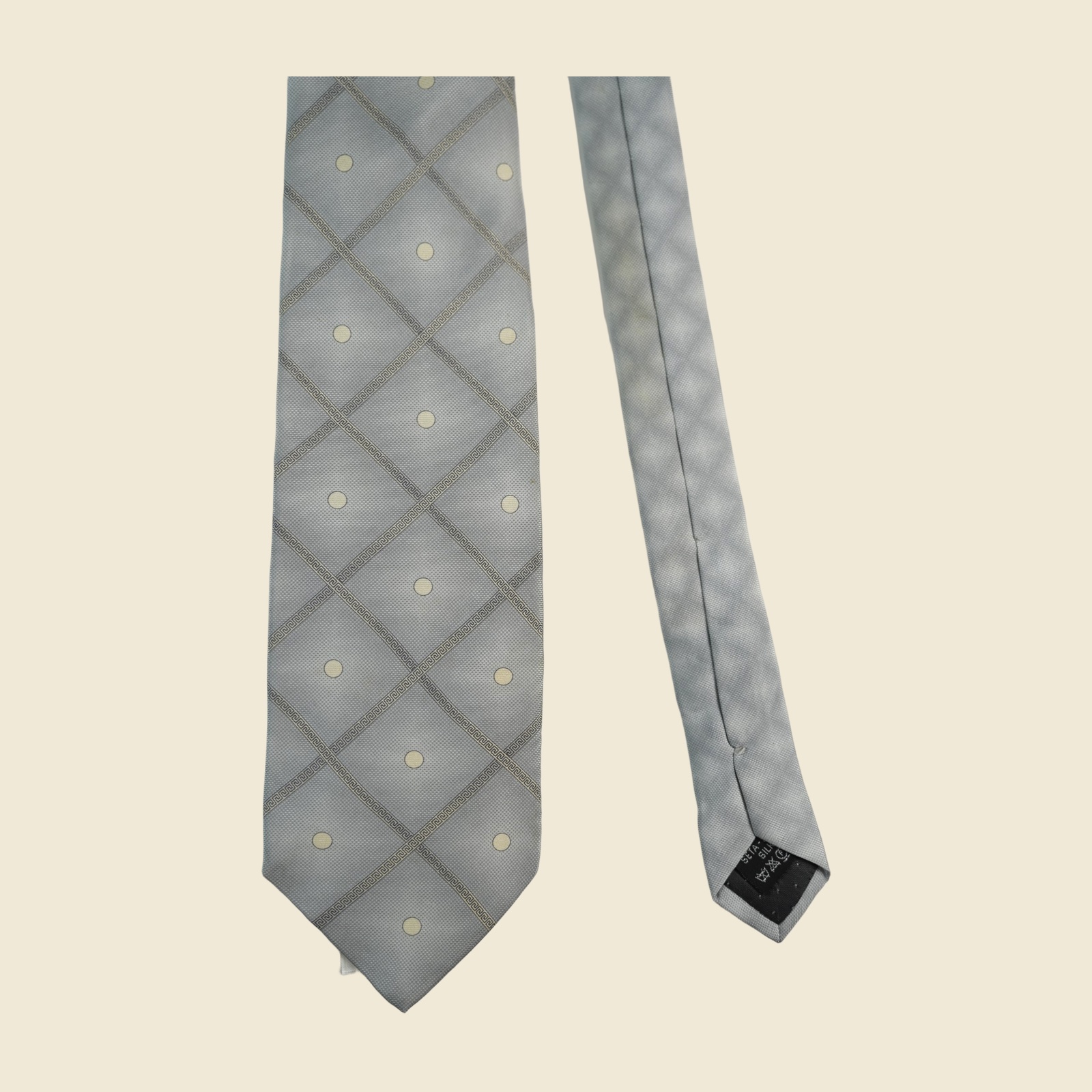Cravatta Gianni Versace in seta grigio argento, reticolo diagonale di greca a rombi con pois avorio, su fondo neutro — vista 3
