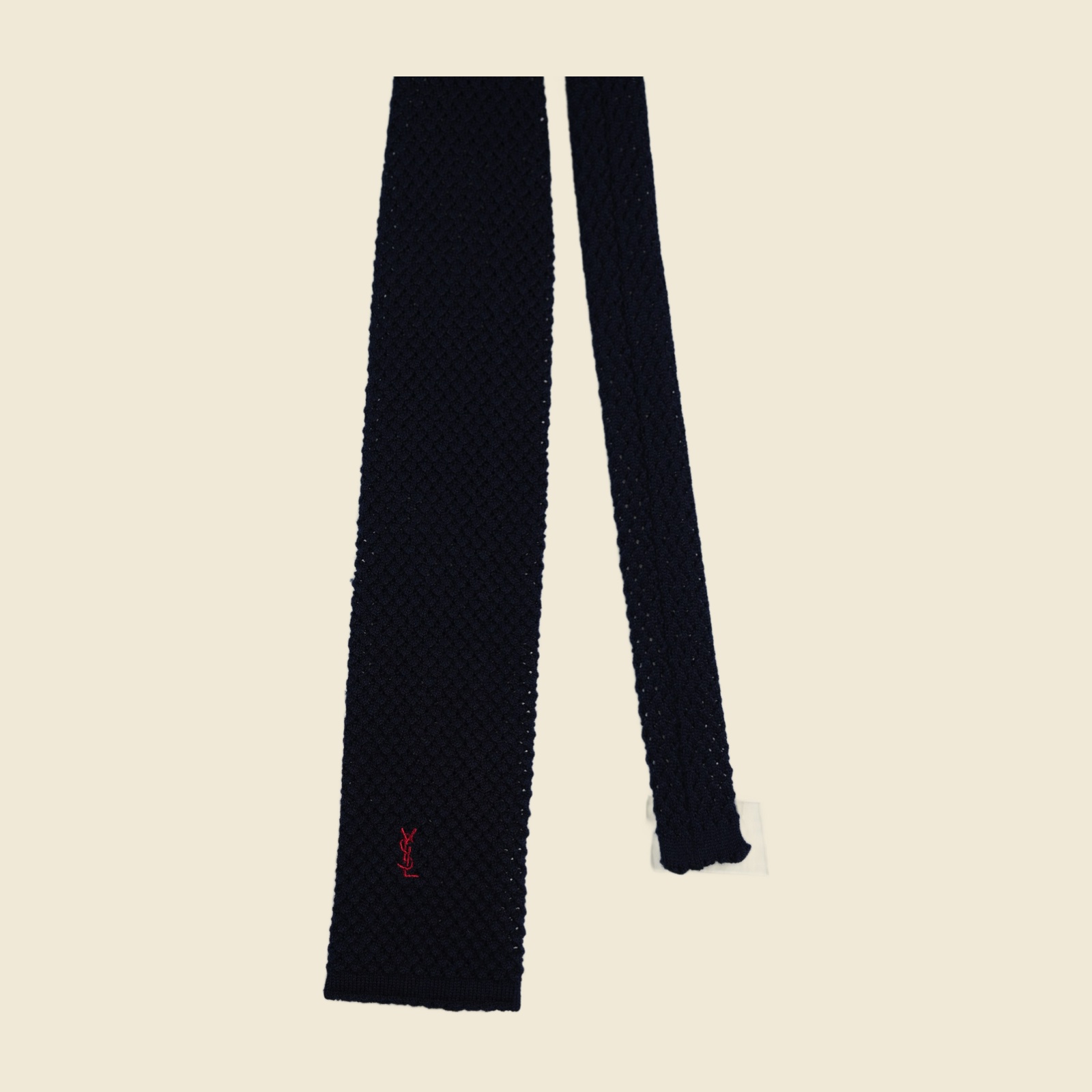 Cravatta Yves Saint Laurent in maglia blu notte a punta quadra, con monogramma YSL ricamato in rosso sul lembo largo, distesa su fondo bianco — vista 2