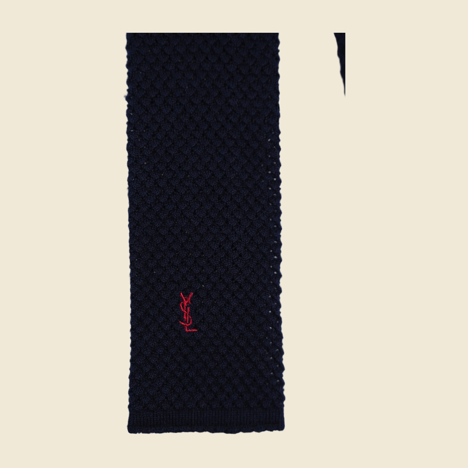 Cravatta Yves Saint Laurent in maglia blu notte a punta quadra, con monogramma YSL ricamato in rosso sul lembo largo, distesa su fondo bianco — vista 3