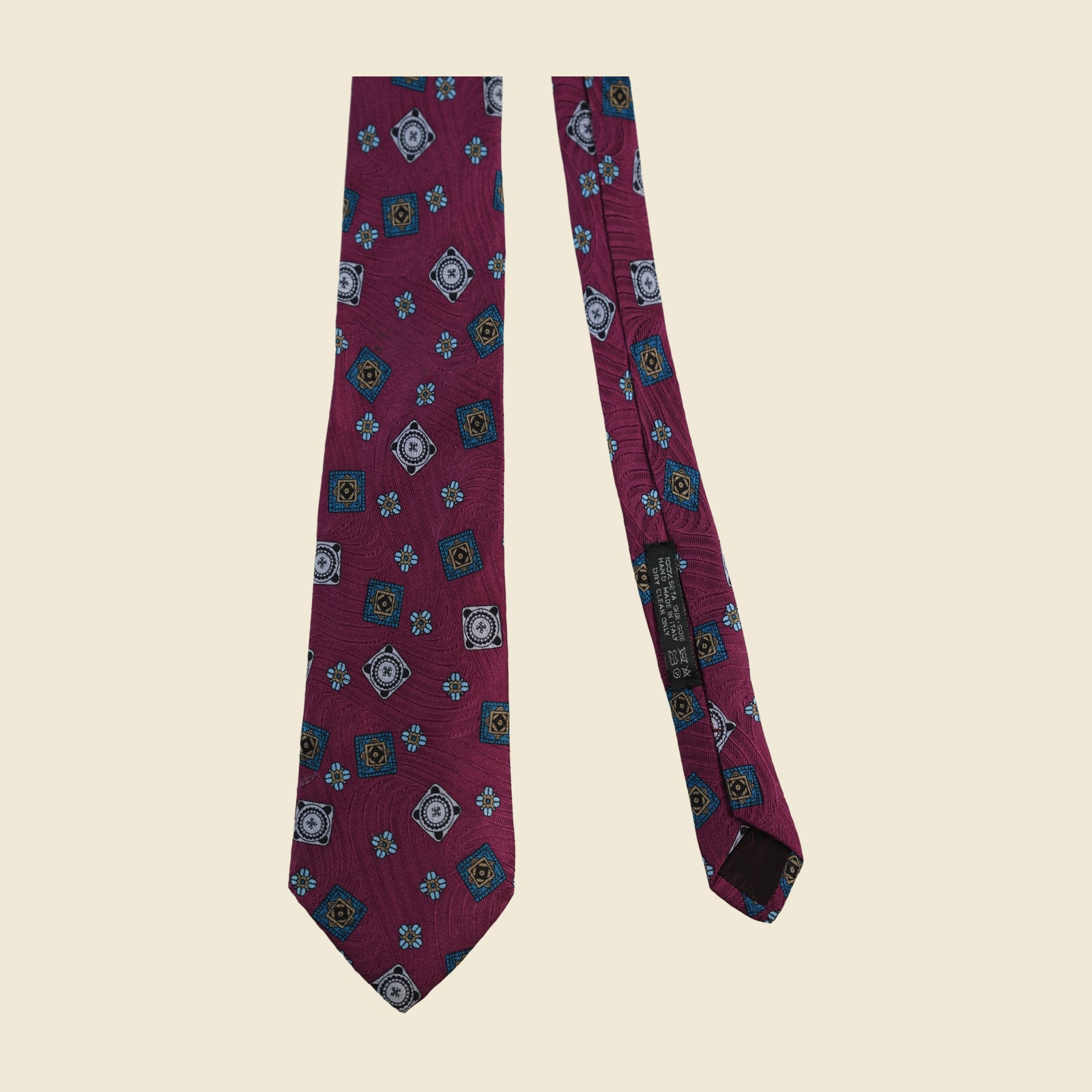 Cravatta Brioni in seta magenta prugna con medaglioni jacquard tessuti in oro, azzurro e ottanio, vista frontale su fondo neutro