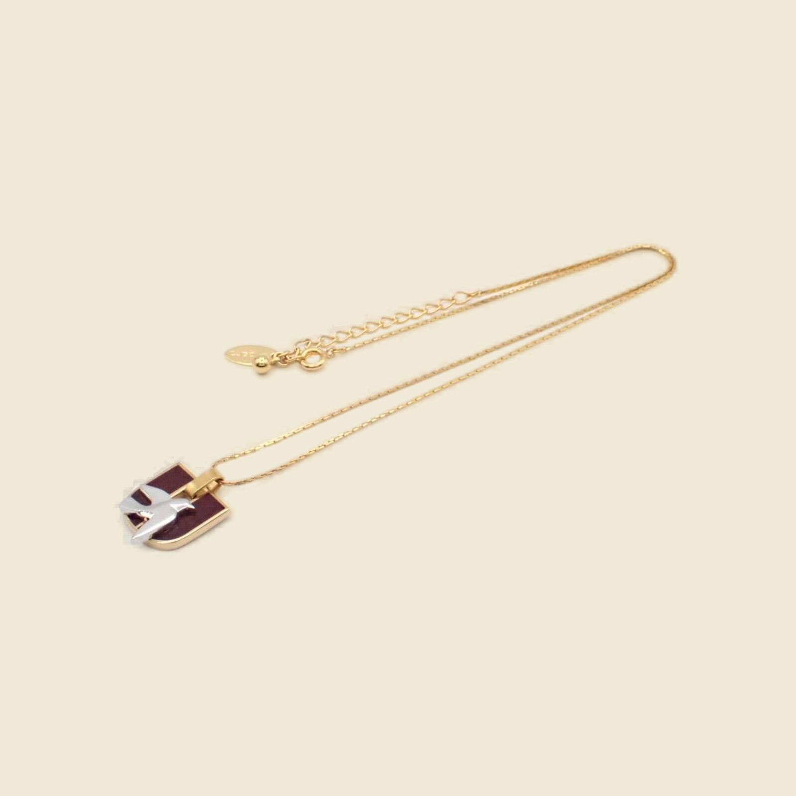 Collana Emanuel Ungaro in metallo dorato con pendente rettangolare in smalto bordeaux e bianco, su fondo neutro