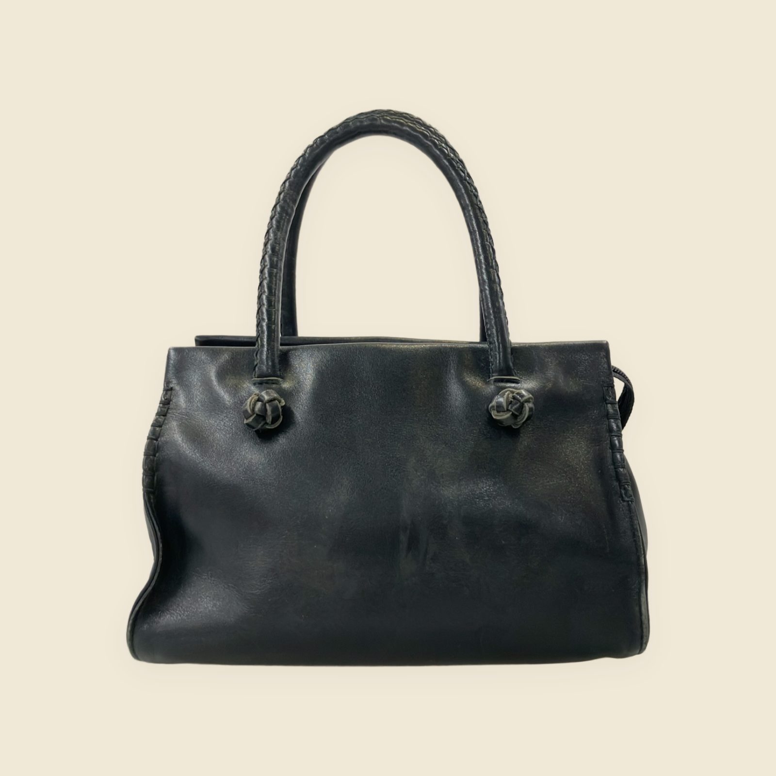 Borsa a mano Kitamura in pelle nera con doppi manici, nodi intrecciati e tasca frontale, vista su fondo neutro