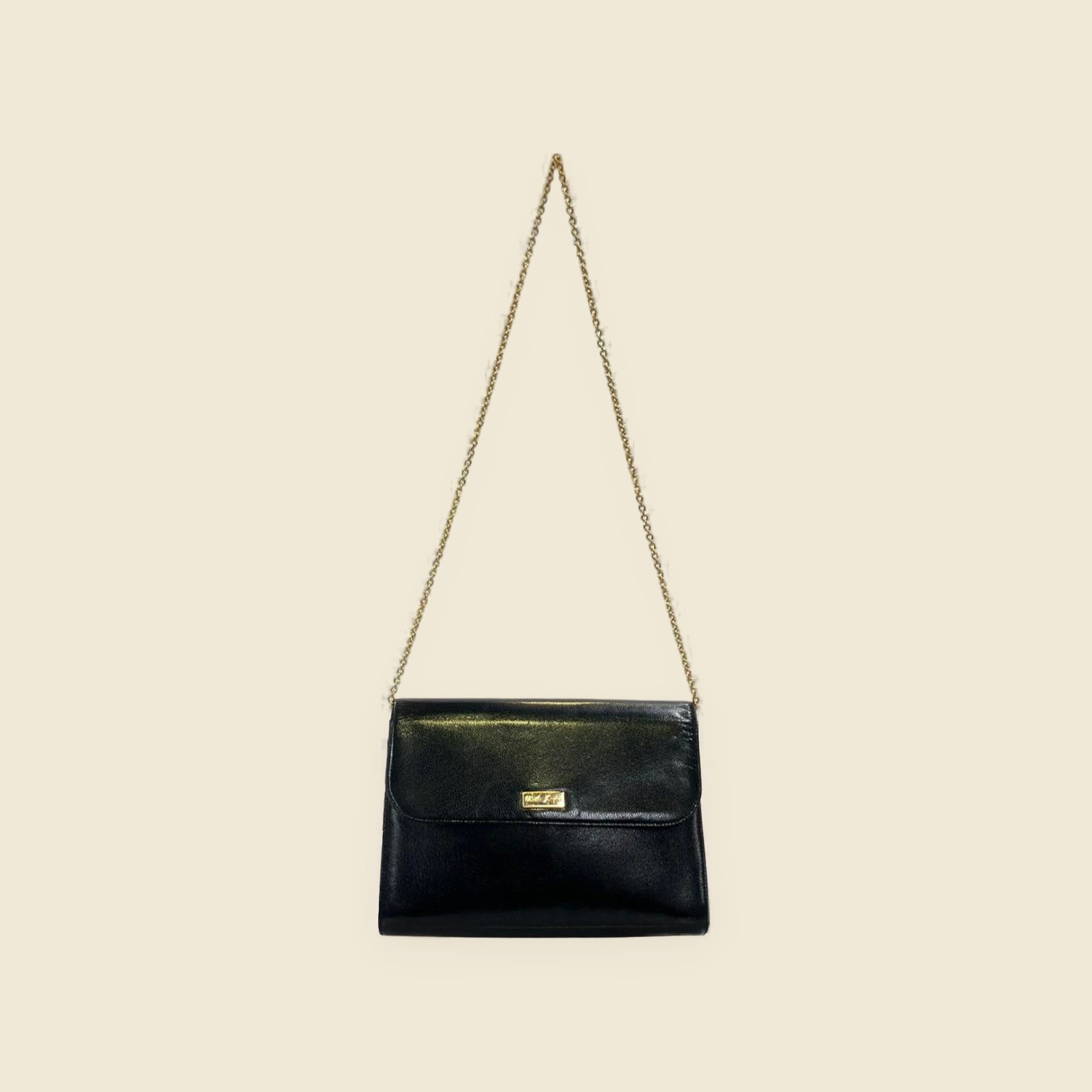 Borsa a spalla in pelle nera con patta, placchetta dorata e tracolla a catena, vista frontale su fondo bianco